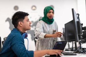 multietnisk börja företag team arab kvinna bär en hijab på möte i modern öppen planen kontor interiör brainstorming, arbetssätt på bärbar dator och skrivbordet dator. selektiv fokus foto