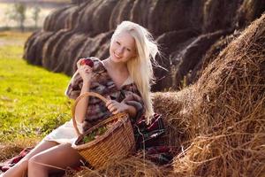 vacker blond kvinna med äpple på höbunken på gården
