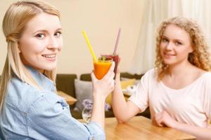 två kvinnor klirrande glas med cocktails i caféet