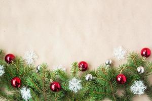 festlig jul gräns med röd och silver- bollar på gran grenar och snöflingor på rustik beige bakgrund foto