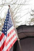 de amerikan flagga i främre av de hus mot de bakgrund av en bladlösa träd i vinter. foto