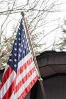 de amerikan flagga i främre av de hus mot de bakgrund av en bladlösa träd i vinter. foto