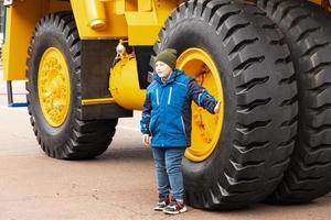 minsk, belarus, september 20, 2022- en barn, en pojke, poser mot de bakgrund av en stor gul hjul av en belaz brytning dumpa lastbil. foto