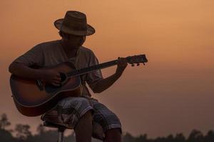 närbild av man i hatt spelar gitarr på solnedgång foto