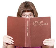 flicka med glasögon utseende över engelsk ordbok foto