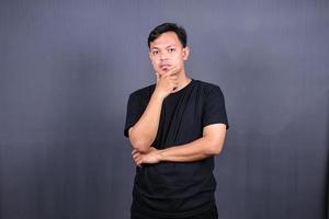 ung asiatisk man innehar haka och utseende stött på kamera känner arg vaknar i dålig humör isolerat över grå bakgrund foto