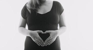 ung vuxen gravid kvinna i vit kläder rörande stor naken mage med händer. som visar form. graviditet begrepp. förväntan tid. närbild. isolerat på ljus grå vägg bakgrund. foto