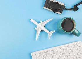 platt lägga av flygplan modell, dator tangentbord, kamera och blå kopp av svart kaffe på blå bakgrund, företag och reser begrepp. foto