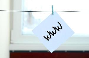 www. notera är skriven på en vit klistermärke den där hänger med en klädnypa på en rep på en bakgrund av fönster glas foto