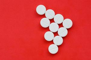 flera vit tabletter lögn på en ljus röd bakgrund i de form av en triangel- pil. bakgrund bild på medicin och farmaceutisk ämnen foto