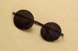 eleganta svart solglasögon med runda glasögon lögner på en filt tillverkad av mjuk och fluffig ljus orange skinna tyg. modern bakgrund bild i mode färger foto