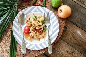 thai papaya sallad på en tallrik, papaya sallad med bajs, citron, peppar, röd tomat i vit skål på trä- tabell foto