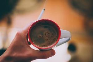 hand som håller cigarett och kaffe i mugg foto