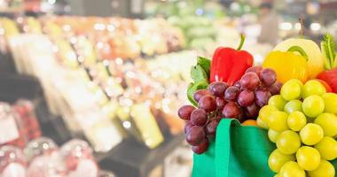 färska frukter och grönsaker i återanvändbar grön shoppingpåse med snabbköp livsmedelsbutik suddig ofokuserad bakgrund med bokeh ljus foto