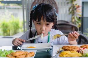 liten flicka asiatisk äta friterad ägg på maträtt på tabell. foto