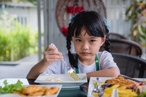 liten flicka asiatisk äta friterad ägg på maträtt på tabell. foto