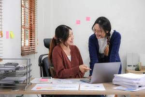 två ung asiatisk kvinna diskutera investering projekt arbetssätt och planera strategi. företag människor talande tillsammans med bärbar dator dator på Hem. foto