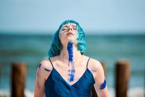 konstnärlig blåhårig kvinna performance artist insmord med blå gouache färger dans på stranden foto