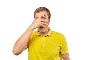 rädd ung kille ser genom fingrar i gul polo t-shirt, vit isolerat bakgrund foto
