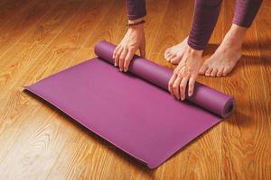 en flicka lägger ut en lila yoga matta innan en träna öva på Hem på en trä- golv. foto
