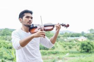 ung hipster musiker man spelar fiol i naturen utomhus livsstil bakom berget. foto