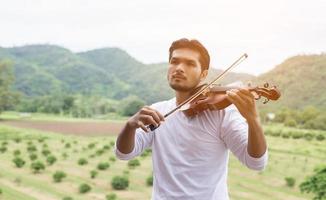 ung hipster musiker man spelar fiol i naturen utomhus livsstil bakom berget. foto