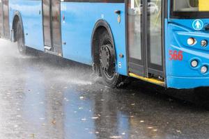 regn vatten stänk strömma från hjul av blå trolleybuss rör på sig i dagsljus stad foto