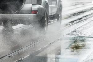 regn vatten stänk strömma från hjul av silver- crossover bil rör på sig snabb i dagsljus stad med selektiv fokus foto
