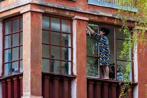 tula, ryssland - Maj 1, 2014, orädd modig vuxen kvinna tvättning fönster av blacony från utanför på tredje golv höjd. foto