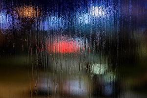 ett abstrakt bakgrund natt gata lampor bokeh genom våt glas, närbild med selektiv fokus foto