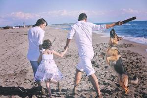 Lycklig familj spelar med hund på strand foto