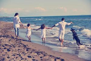 Lycklig familj spelar med hund på strand foto