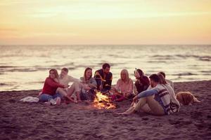 grupp av ung vänner Sammanträde förbi de brand på strand foto