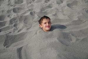 Lycklig barn begravd i sand foto