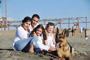 Lycklig familj spelar med hund på strand foto