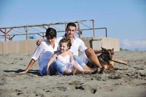 Lycklig familj spelar med hund på strand foto
