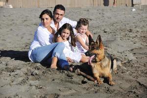 Lycklig familj spelar med hund på strand foto