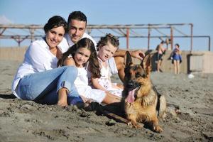 Lycklig familj spelar med hund på strand foto