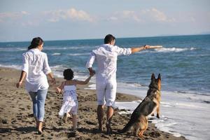 Lycklig familj spelar med hund på strand foto