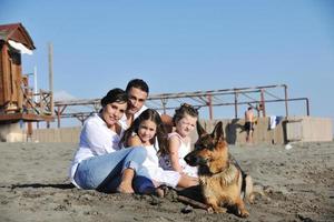 Lycklig familj spelar med hund på strand foto