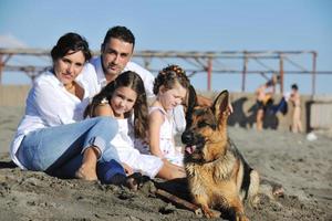 Lycklig familj spelar med hund på strand foto