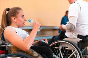 en kvinna rullstol basketboll spelare sitter i ett invlad rullstol på en ha sönder och drycker vatten. foto