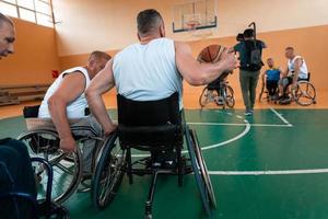 Inaktiverad krig veteraner blandad lopp och ålder basketboll lag i rullstolar spelar en Träning match i en sporter Gym hall. handikappade människor rehabilitering och inkludering begrepp foto