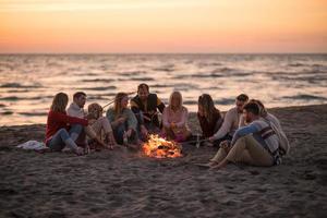 grupp av ung vänner Sammanträde förbi de brand på strand foto