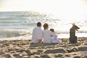 Lycklig familj spelar med hund på strand foto