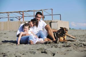 Lycklig familj spelar med hund på strand foto