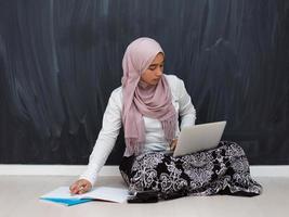 arab tonåring med hijab Sammanträde på de golv av de hus och tittar på uppkopplad klasser under de coronavirus pandemisk. selektiv fokus foto