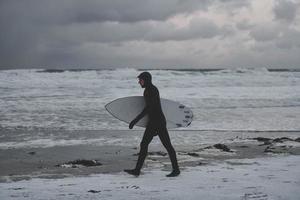 arktisk surfare gående förbi strand efter surfing foto