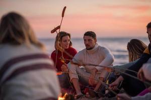 grupp av ung vänner Sammanträde förbi de brand på strand foto