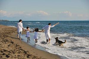 Lycklig familj spelar med hund på strand foto